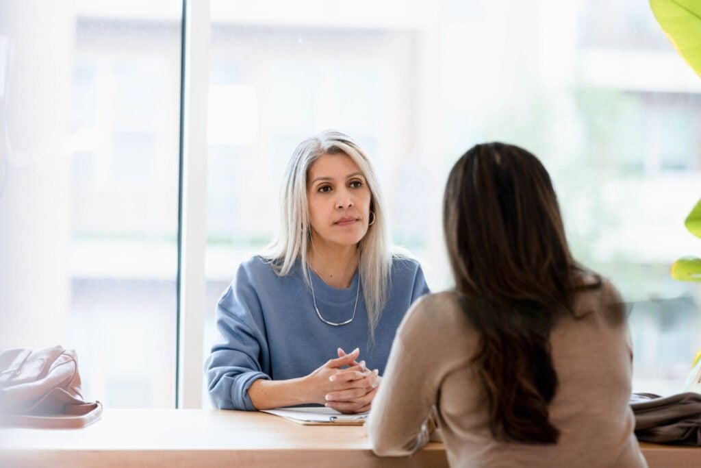 Woman attentively listens across a table to another woman during a serious conversation.