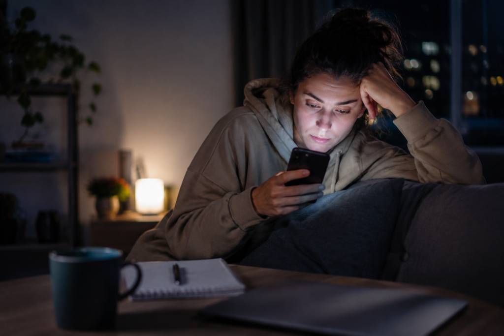Adult woman with ADHD doomscrolling on her phone late at night while sitting on a sofa, showing signs of mental fatigue, distraction and screen overwhelm in a realistic home setting.